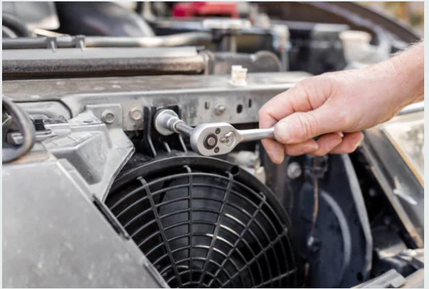 Hand using a ratchet above a vehicle radiator fan assembly
