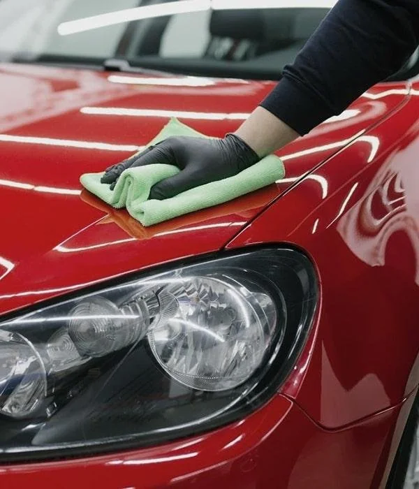 Gloved hand wiping a red Volkswagen bonnet with a microfibre cloth