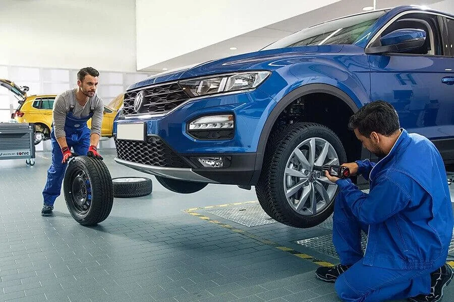 Technicians working beside the front wheel of a blue Volkswagen SUV