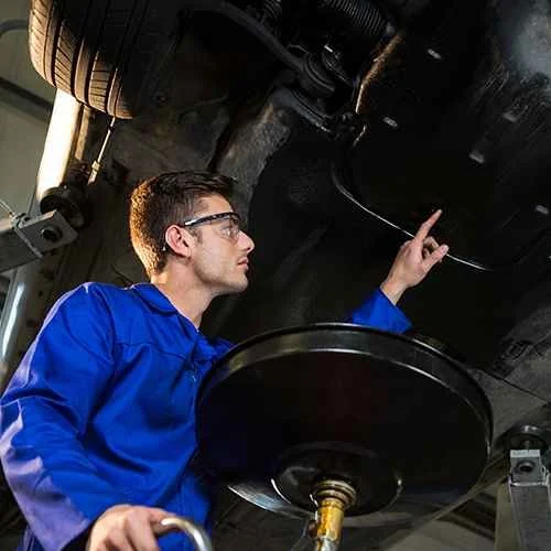 Technician inspecting a vehicle underside above an oil collection bowl